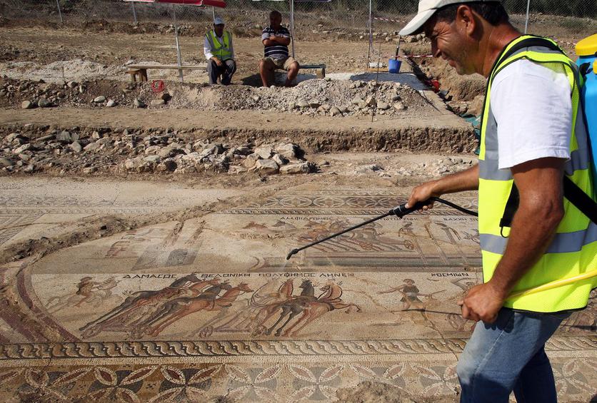 epa05467246 An Antiquities Department staff sprays water on a complete mosaic floor of building remains dated to the first half of the 4th century AD at the Piadhia locality in Akaki village, Nicosia district, Cyprus 09 August 2016. The floor was presented by the Antiquities Department on Tuesday. The floor depicts a chariot scene taking place in the hippodrome. According to archaeologists, the mosaic is unique due to its unparalleled subject matter and high quality. EPA/KATIA CHRISTODOULOU